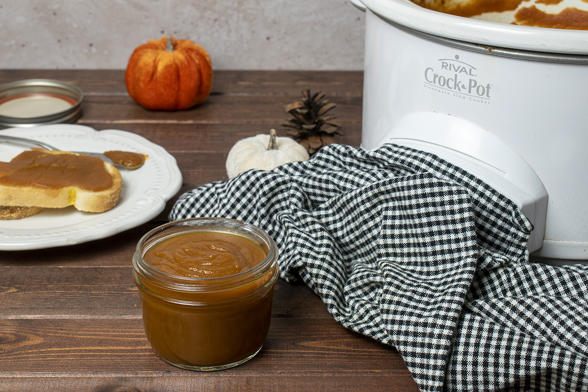 A jar of pumpkin butter next to a slow cooker with more pumpkin butter cooking.
