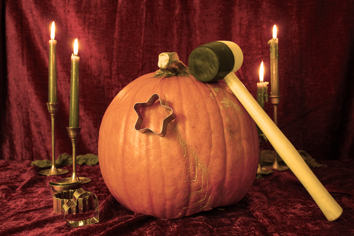 A star-shaped cookie cutter has been hammered into the side of a pumpkin using a wooden mallet.