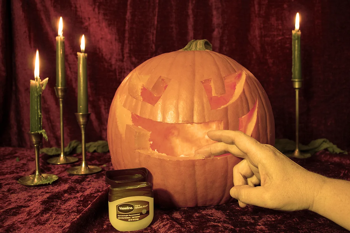Woman's hand shown applying petroleum jelly to the cut edges of a jack-o-lantern.
