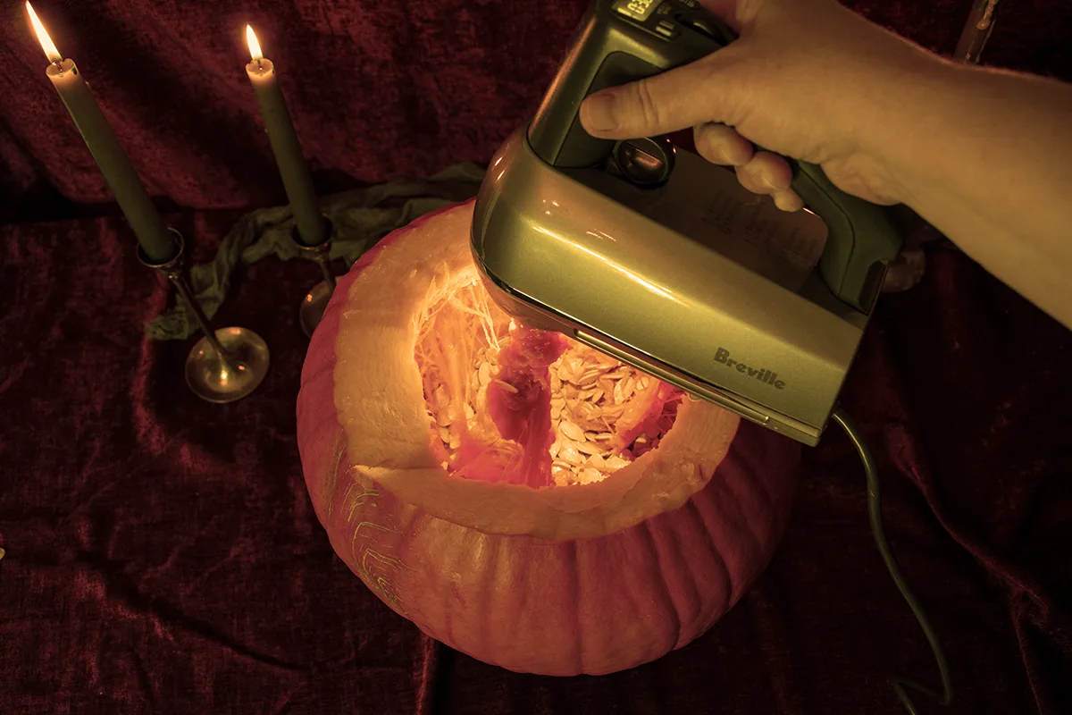 Overhead view of hand mixer being used to scrape out the inside of a pumpkin.
