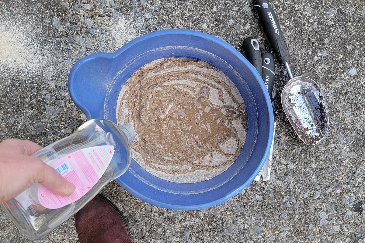 Woman's hand pouring mineral oil in a bucket of sand. 