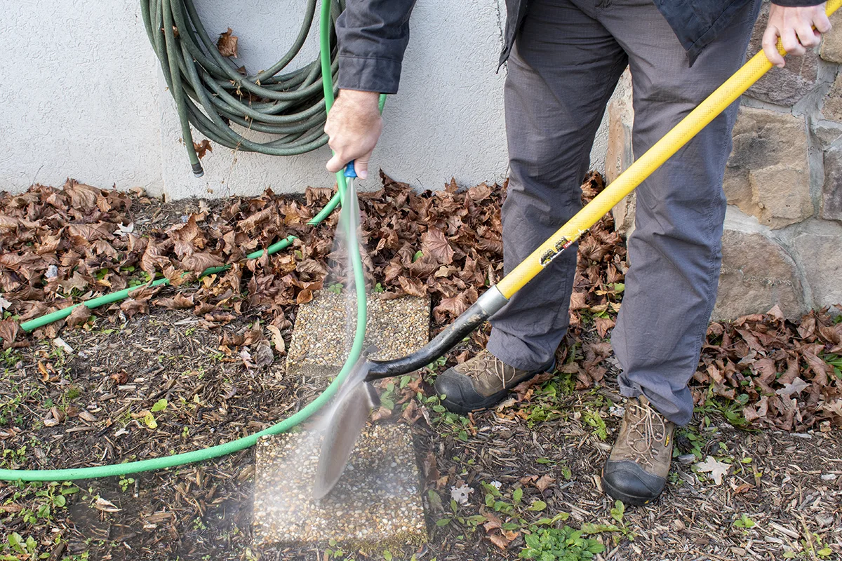 Man spraying shovel with water from garden hose.