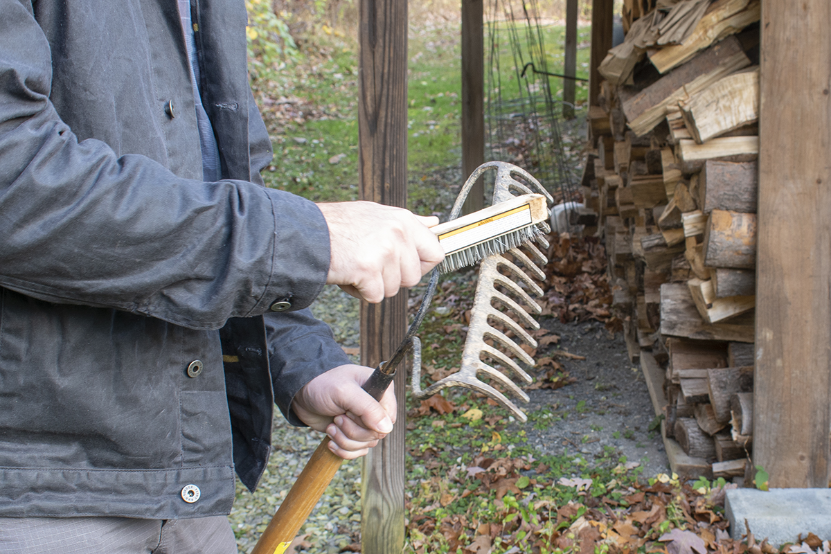 Man brushing rust and dirt off a garden rake.