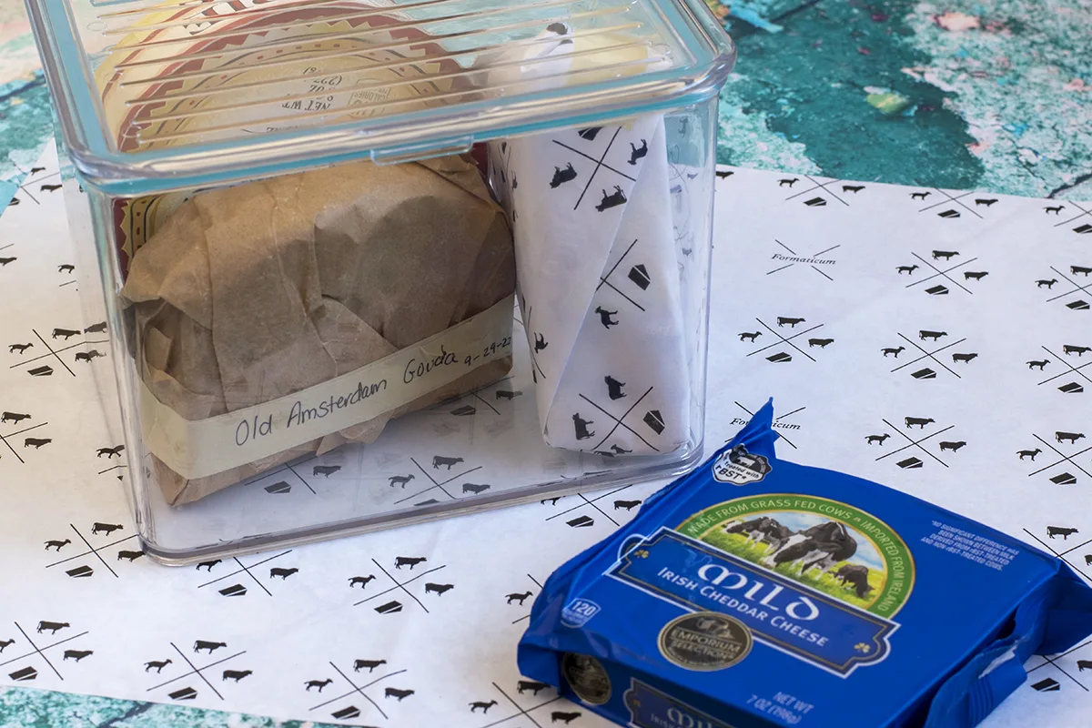 Small plastic airtight box with wrapped cheeses inside it. A small block of mild Irish cheddar cheese in blue packaging.