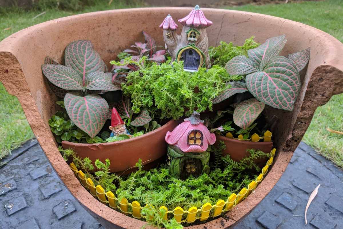 A fairy garden with tiny houses and a gnome set up in a broken pot. 