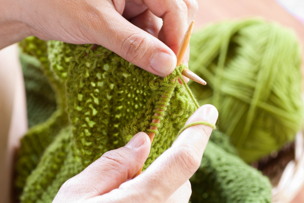 A woman's hands knitting with green yarn.