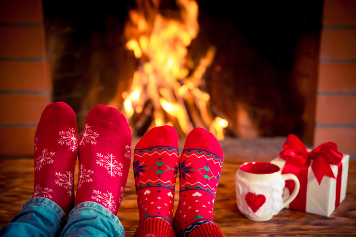 View of two pairs of feet on a coffee table in front of a fireplace. Mug and gift on the table.