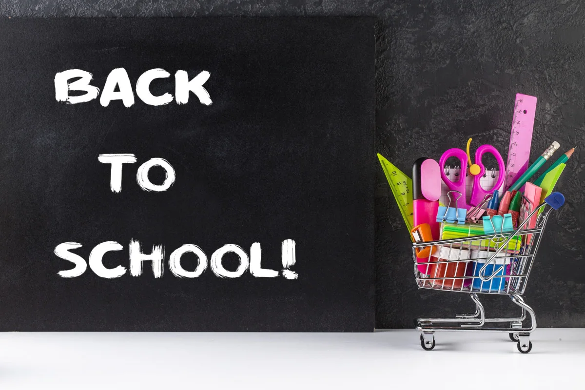 "Back to School!" written on a little chalkboard next to a tiny shopping cart filled with school supplies.