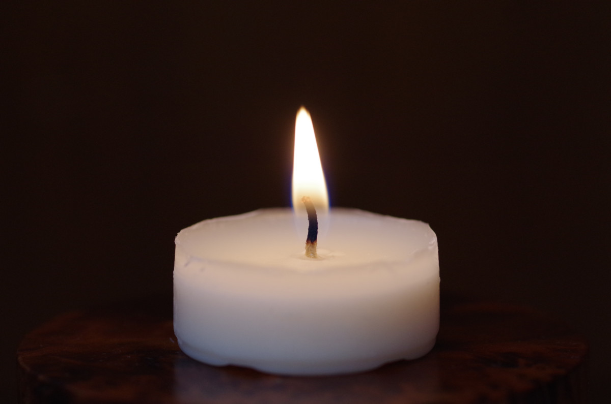 Single tealight candle against a black background. 
