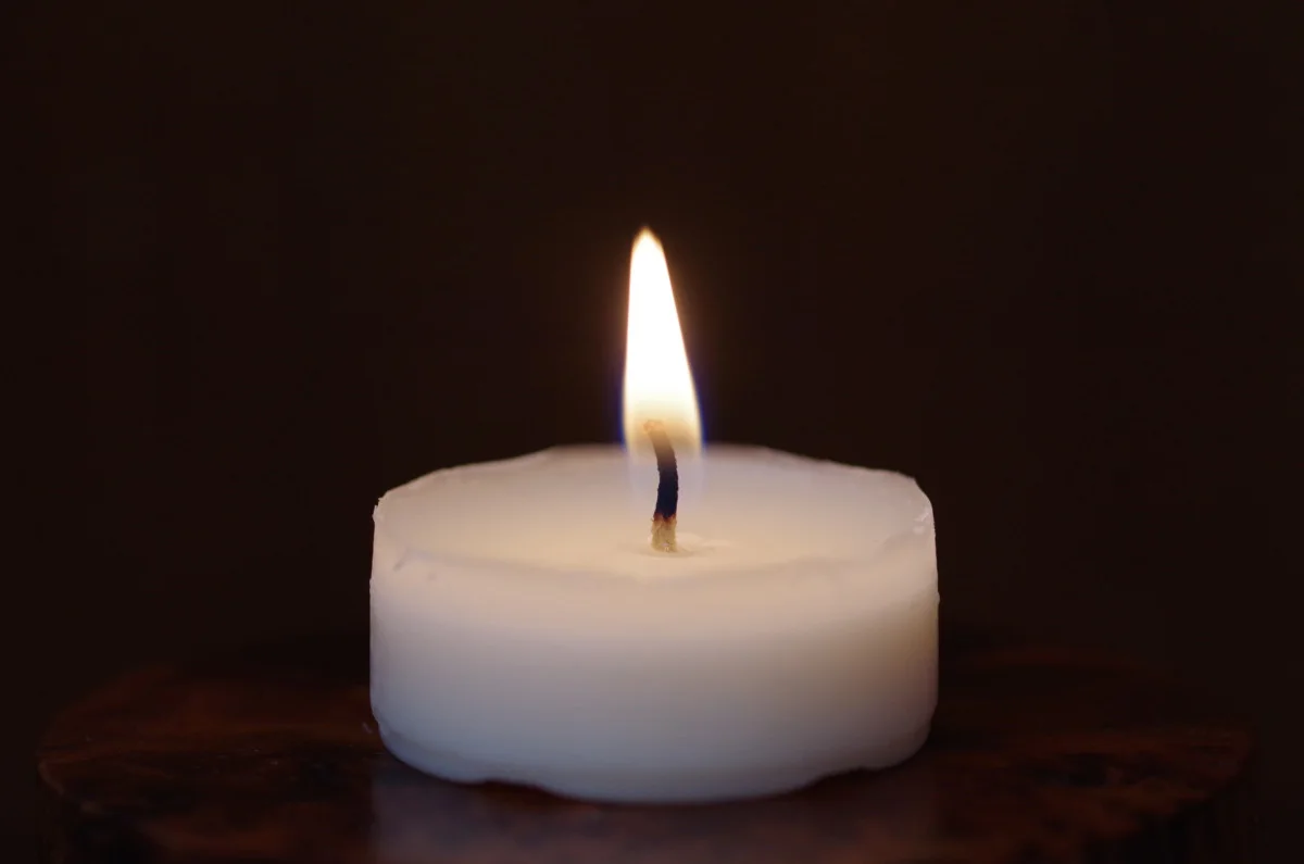 Single tealight candle against a black background. 