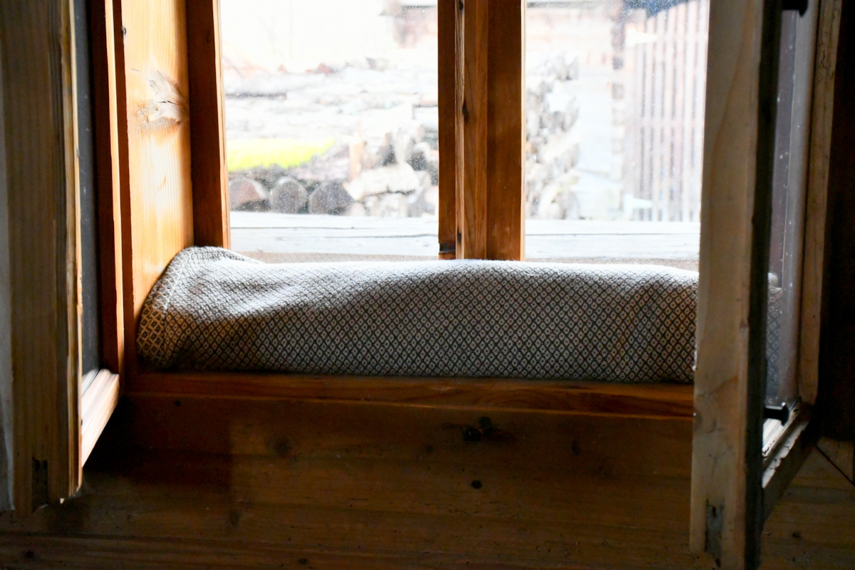 A blanket rolled up and tucked at the base of a window to prevent drafts. 