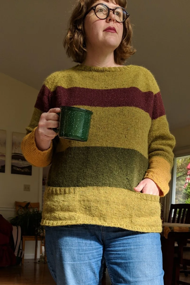 Woman wearing handknit sweater and holding a mug.