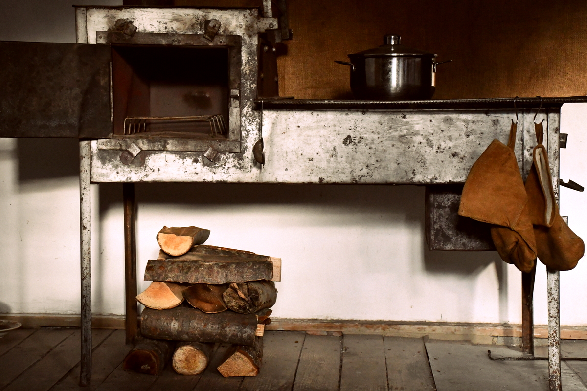 A small cook stove with wood neatly stacked beneath it. 