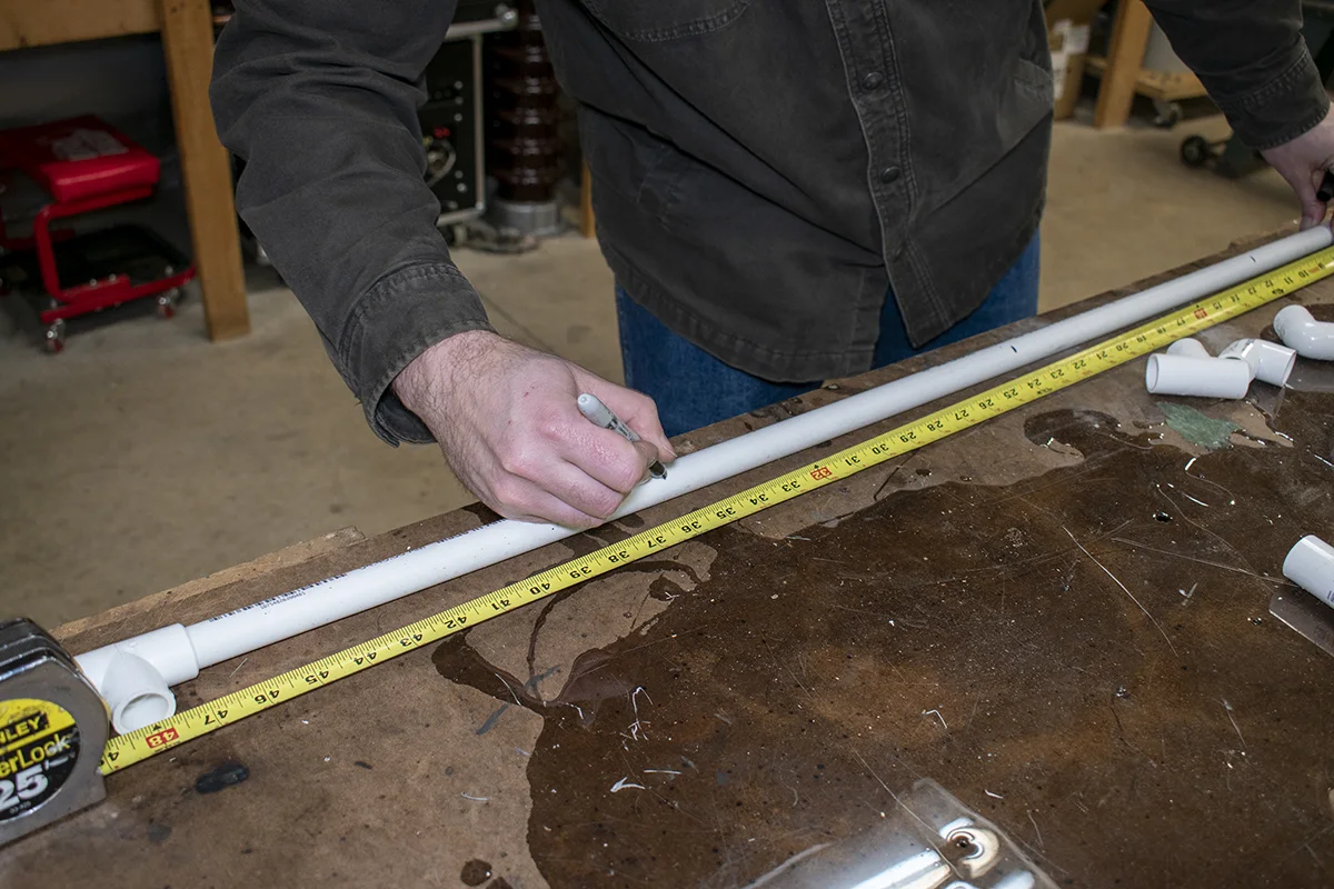 Mans hands shown marking measurements on a piece of pipe.