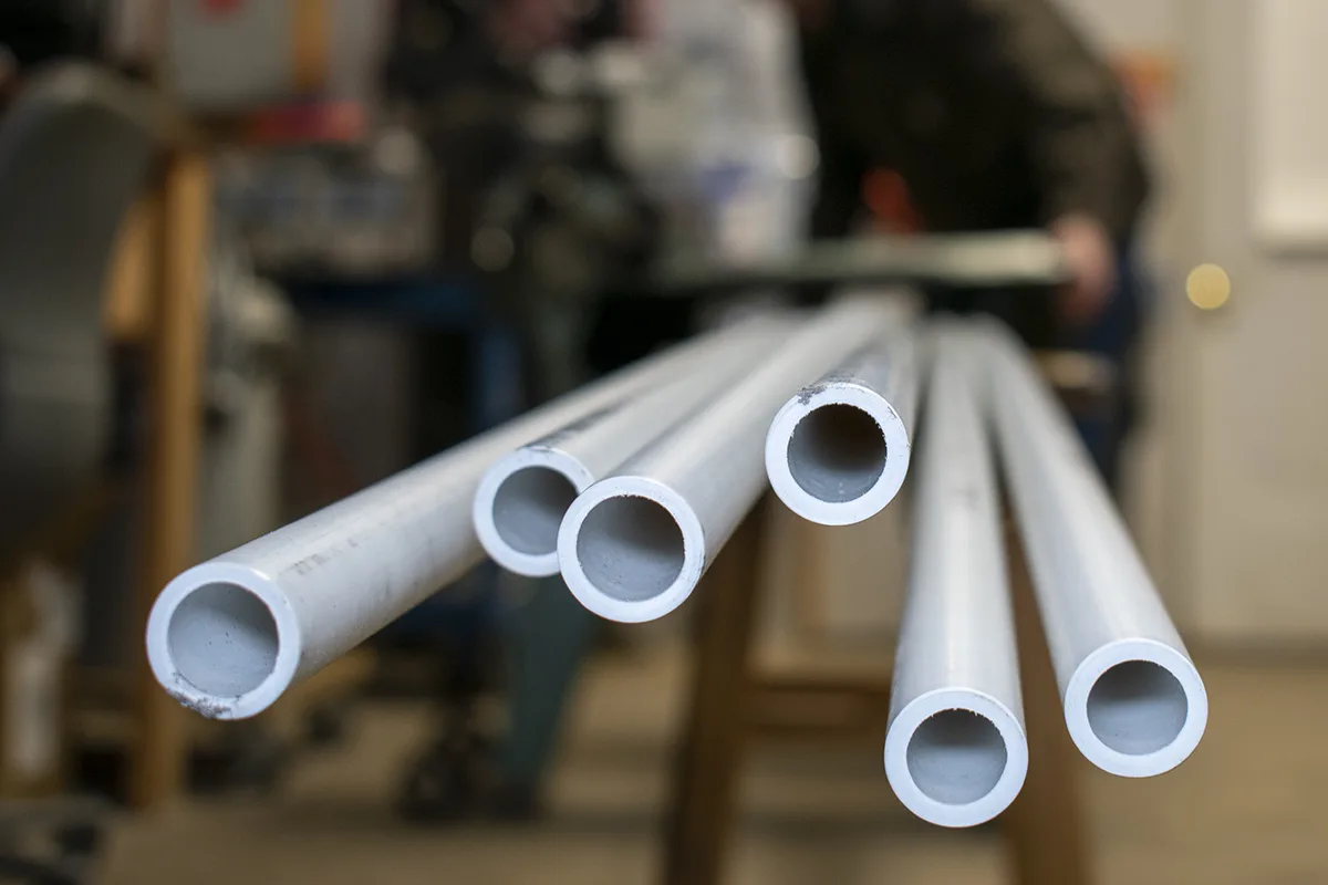 Ends of PVC pipe, soft focus man in background using a bandsaw to cut the pipes.