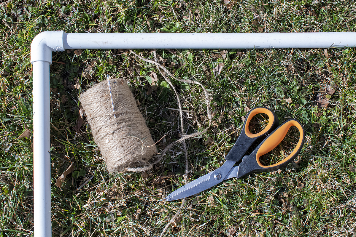 Twine, needle and scissors on the grass next to a PVC frame.