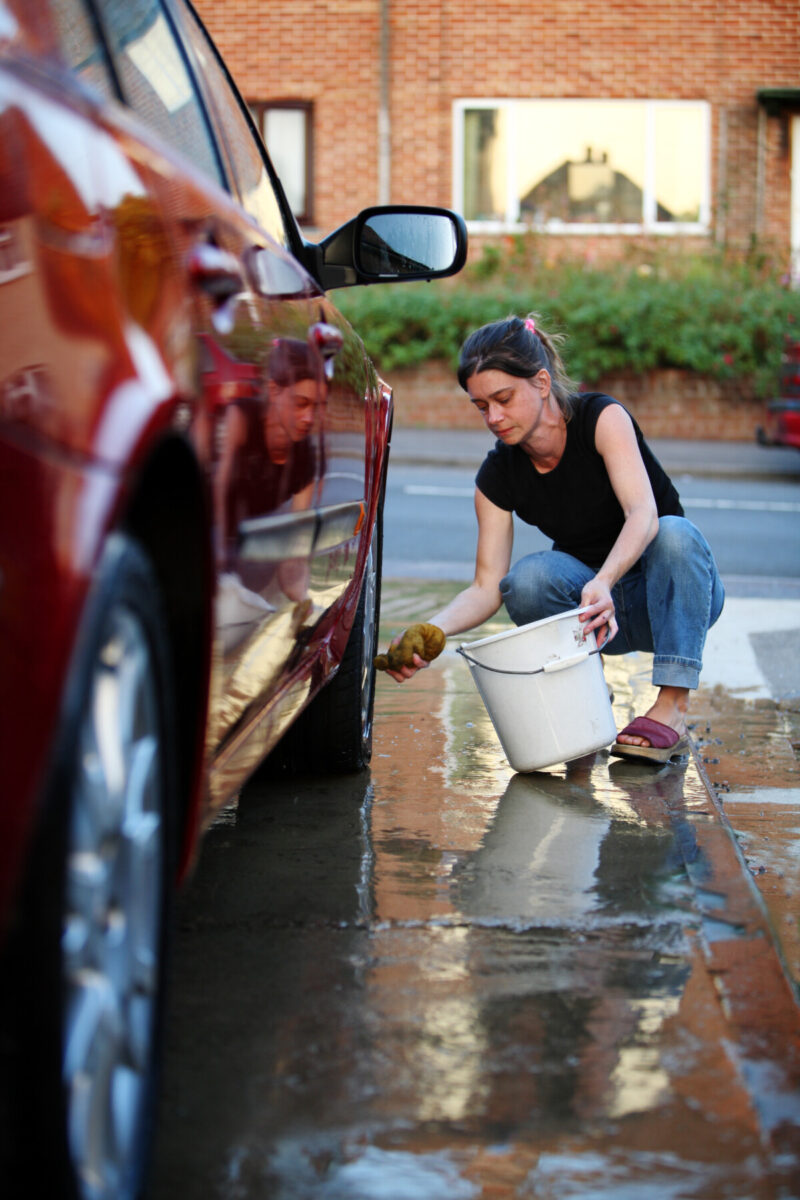 Woman washing her car with a bucket and spone.