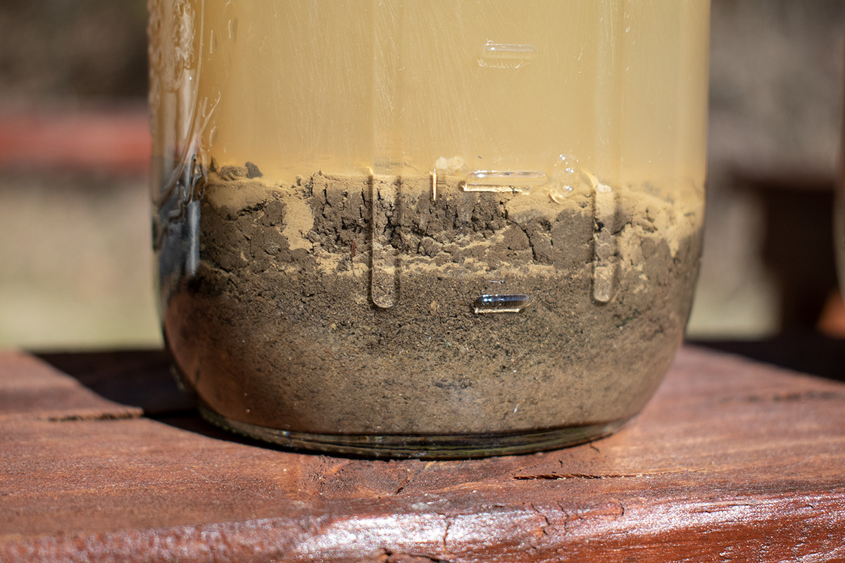 Close up photo of a jar filled with soil and water. 
