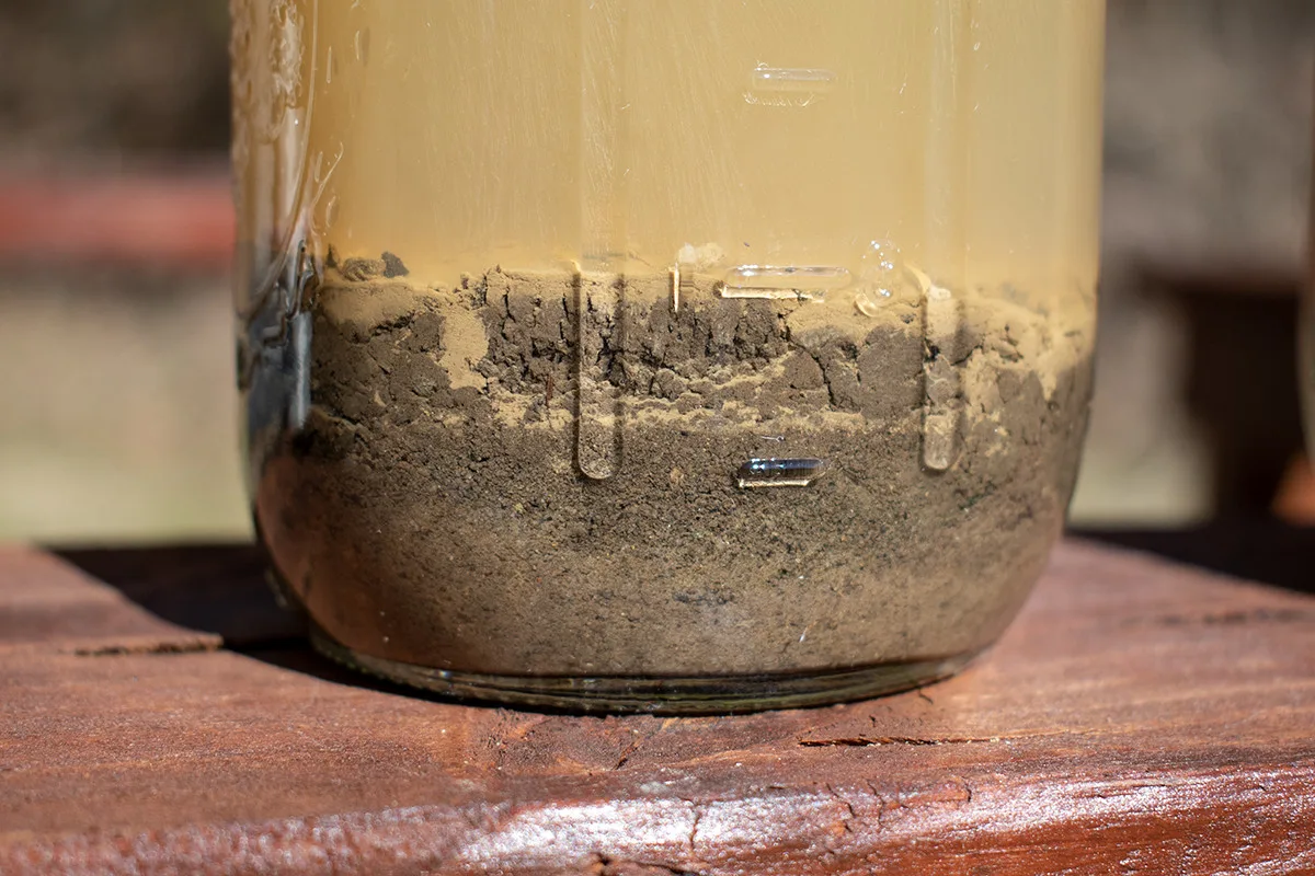 Close up of layers of soil sediment in a jar filled with water.