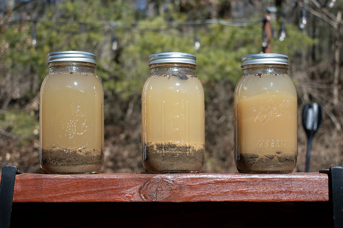 Three jars filled with soil and water sitting on a porch railing in the sun.