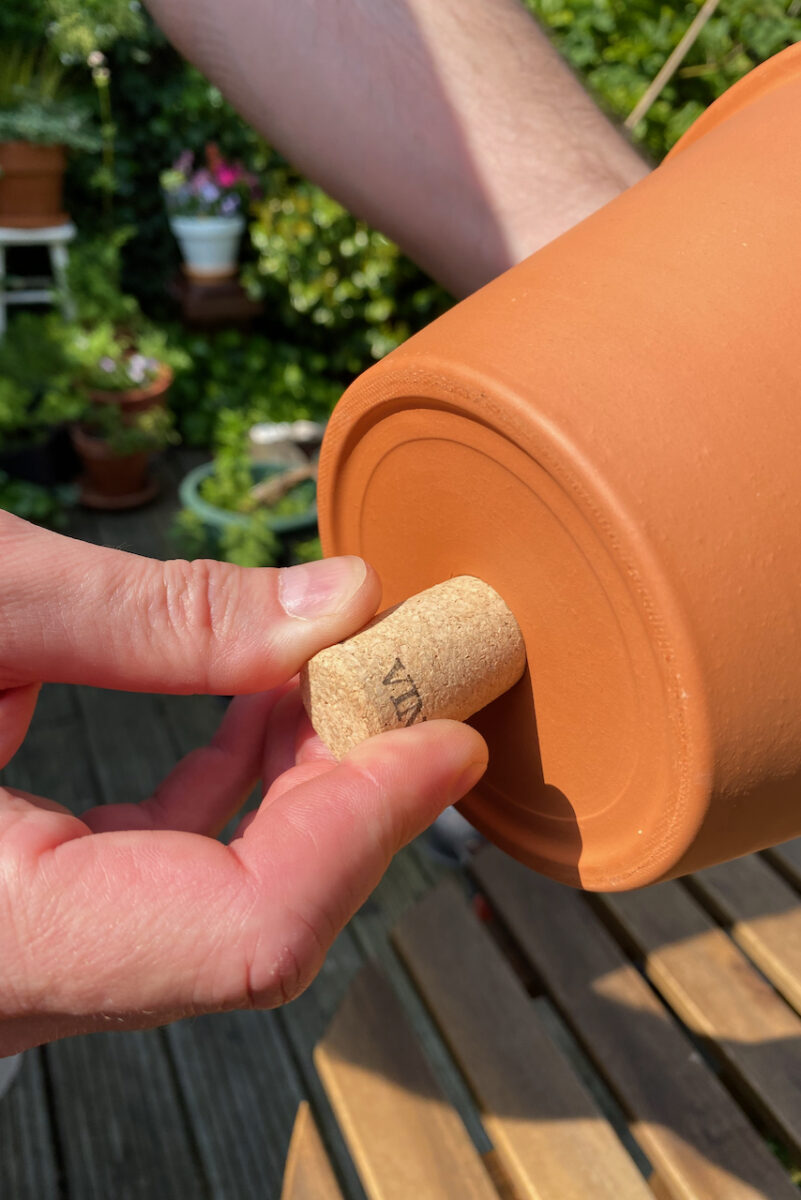 Hand pushing a cork into the drainage hole of a terracotta pot