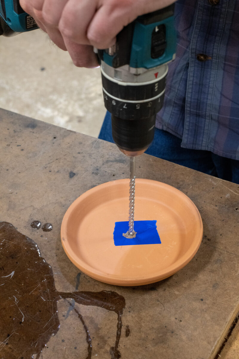 Man's hands using a power drill to drill a hole in a terracotta saucer.