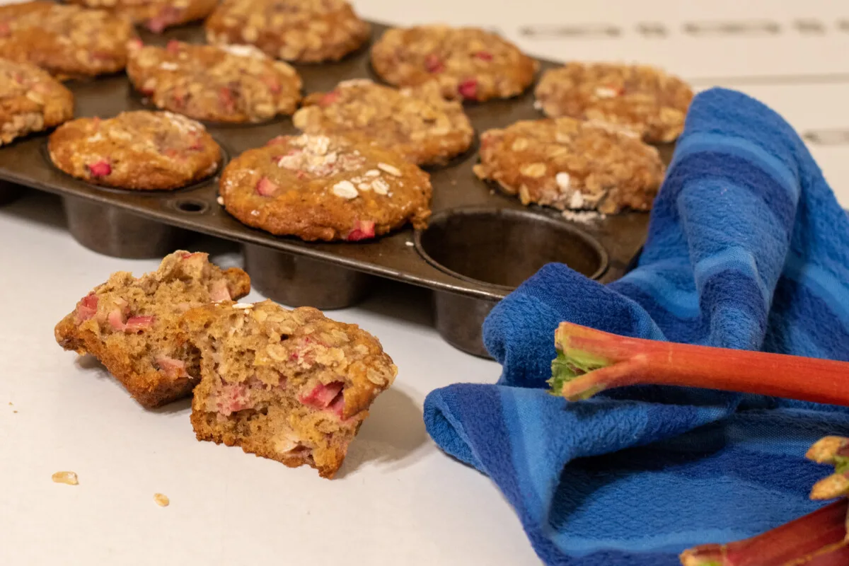 A tin of rhubarb oat muffins with a blue hand towel and a stalk of rhubarb on a table