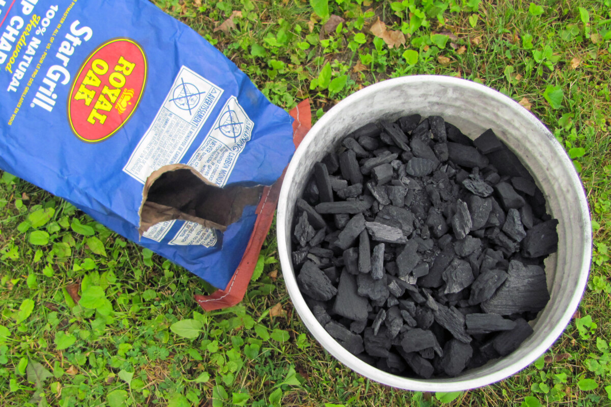 Empty charcoal bag next to a bucket full of lump charcoal