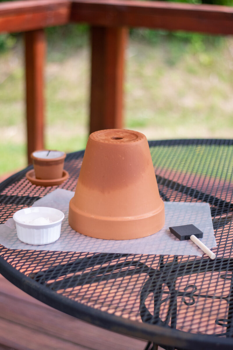 A new terracotta pot on a table outdoors. There is a small white bowl and a foam brush next to the pot.