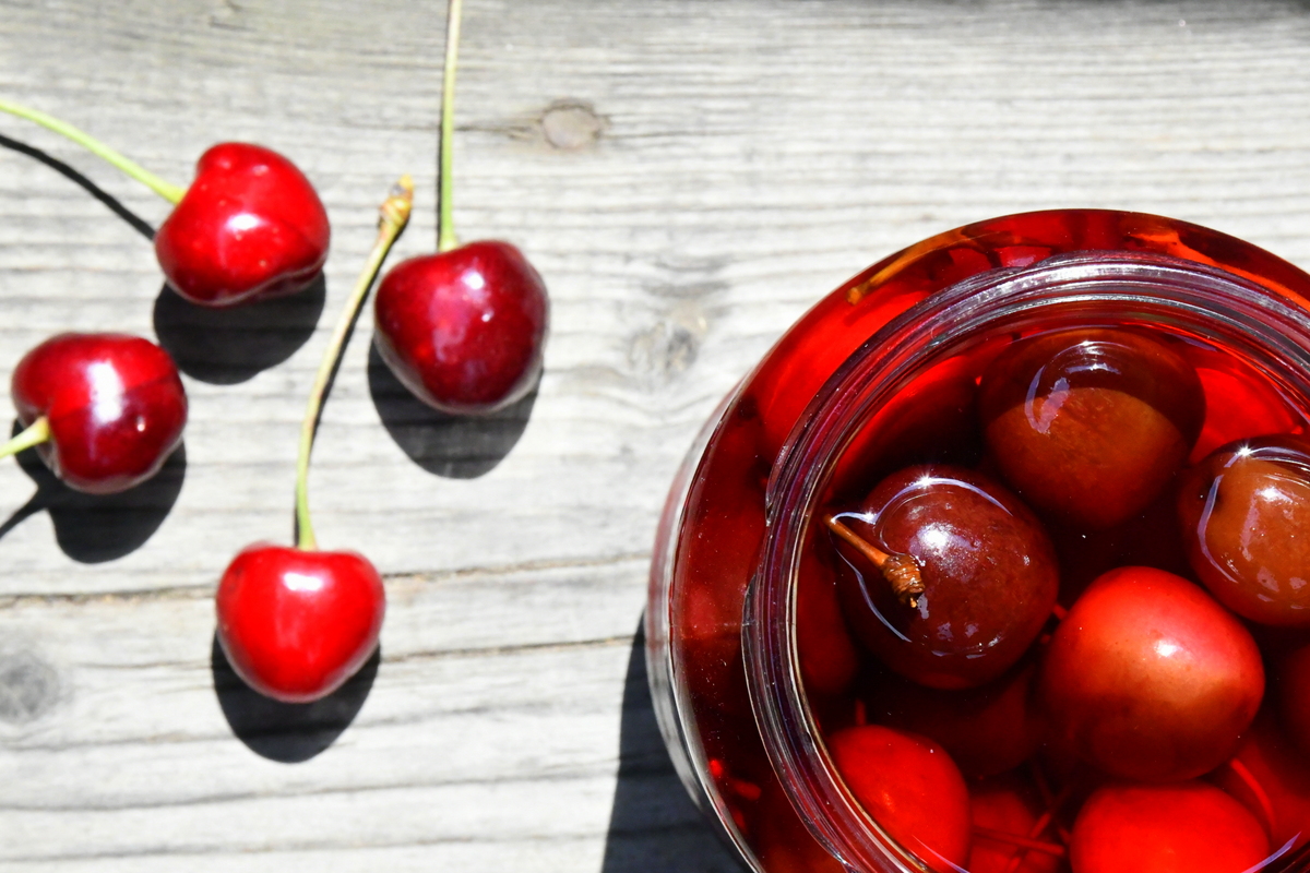 Bright red cherries on wood and brandied cherries in a jar.