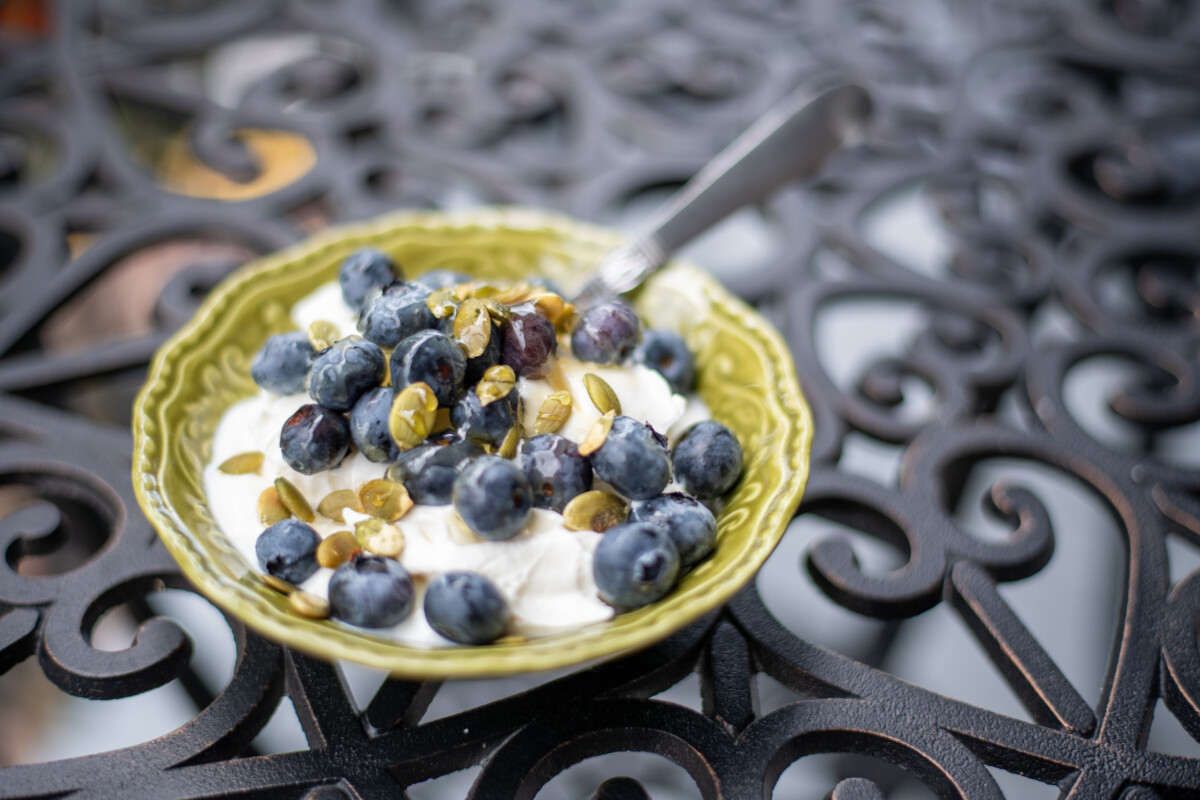 A dish of yogurt topped with blueberries and pumpkin seeds