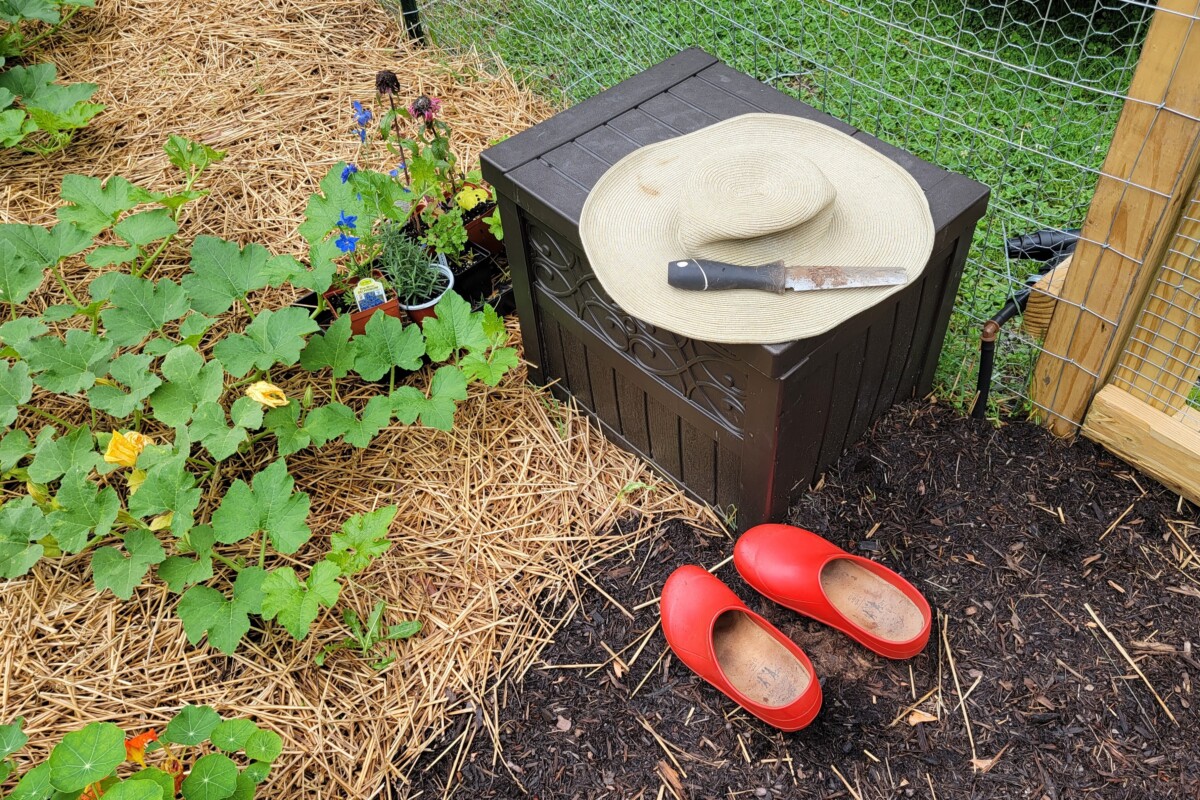 Garden clogs, straw hat and hand tool at the edge of a garden