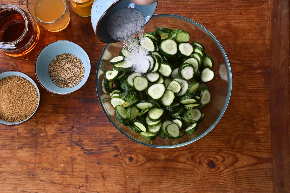 Hand putting salt in a bowl of cucumbers.