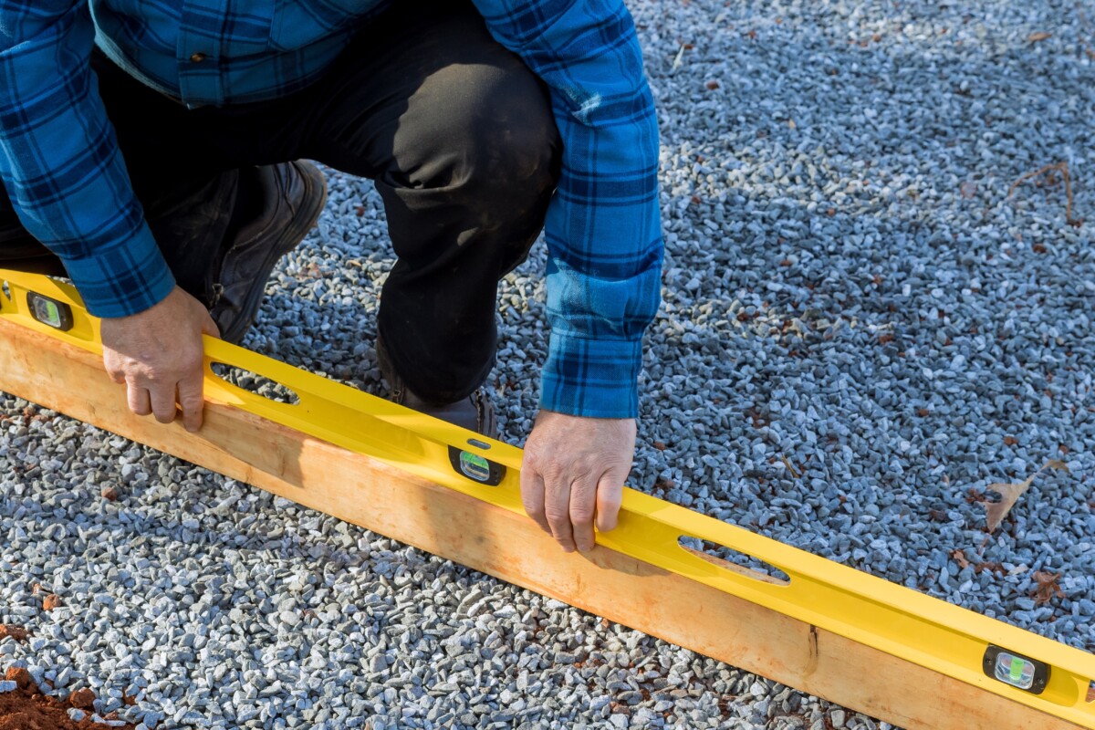 Man using a level on a board set on a gravel foundation