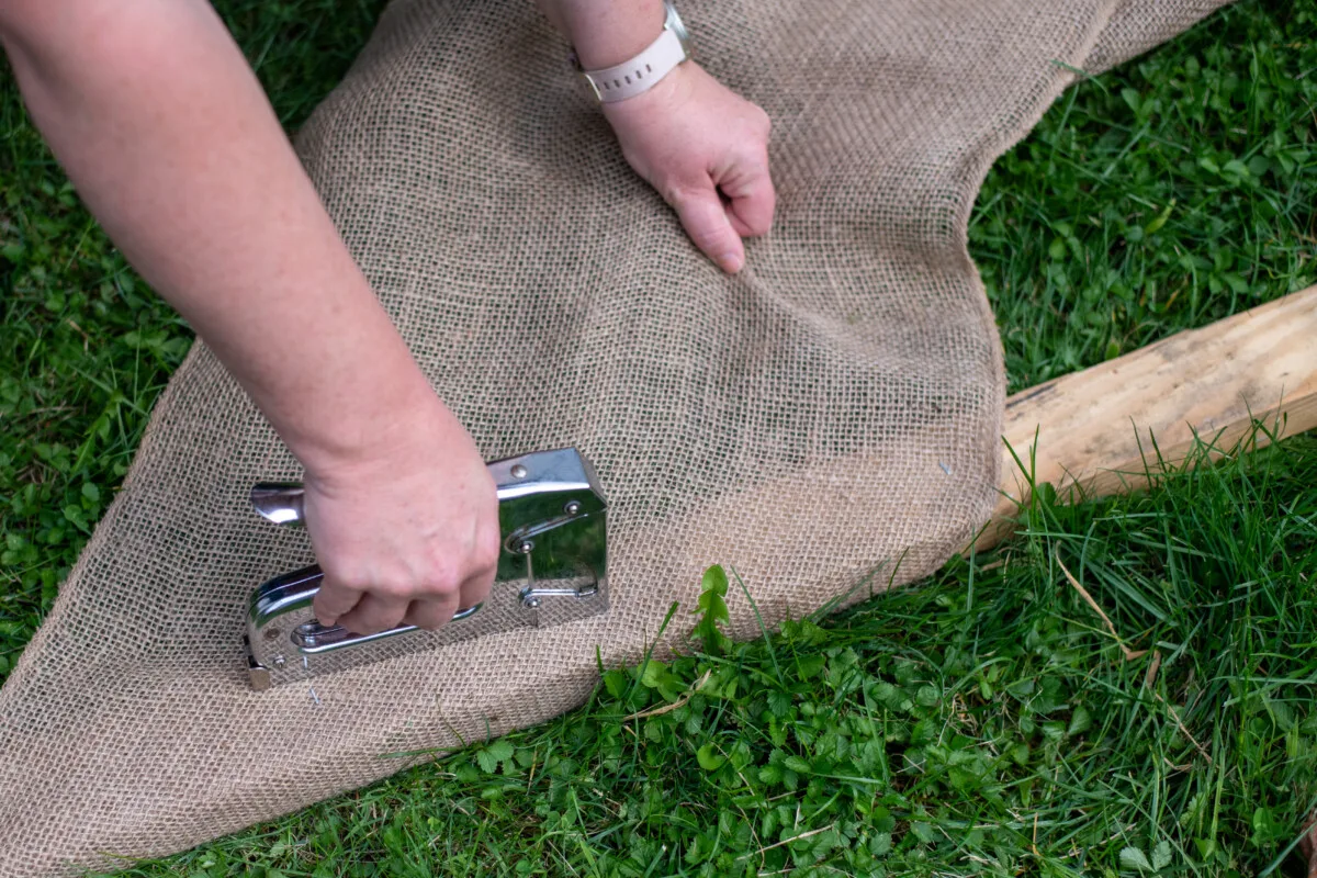 Woman's hands shown using a staple gun to staple burlap to a piece of lumber