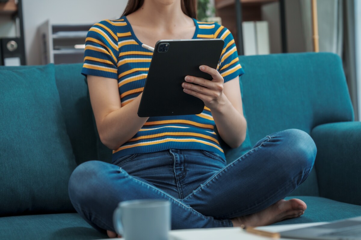 woman's body holding a tablet, sitting on a couch
