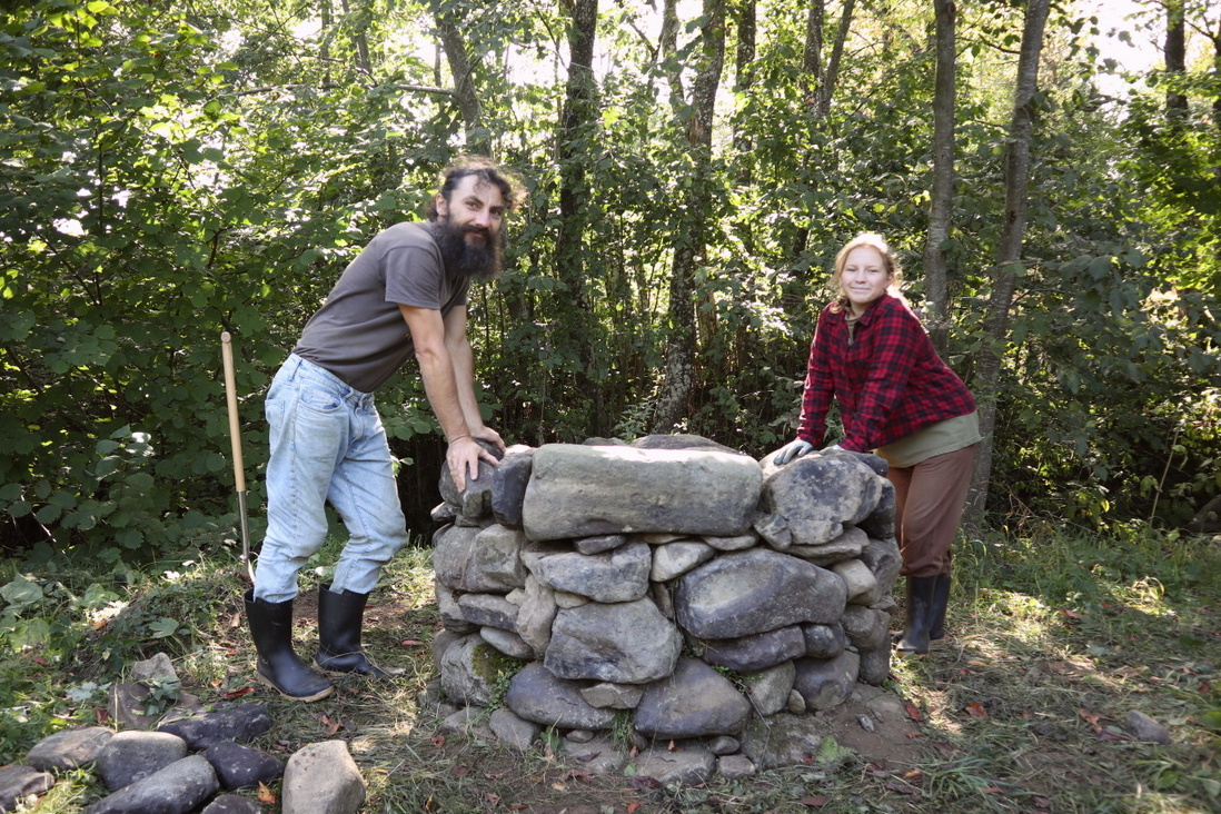 Man and his daughter building a stone foundation for a cob oven