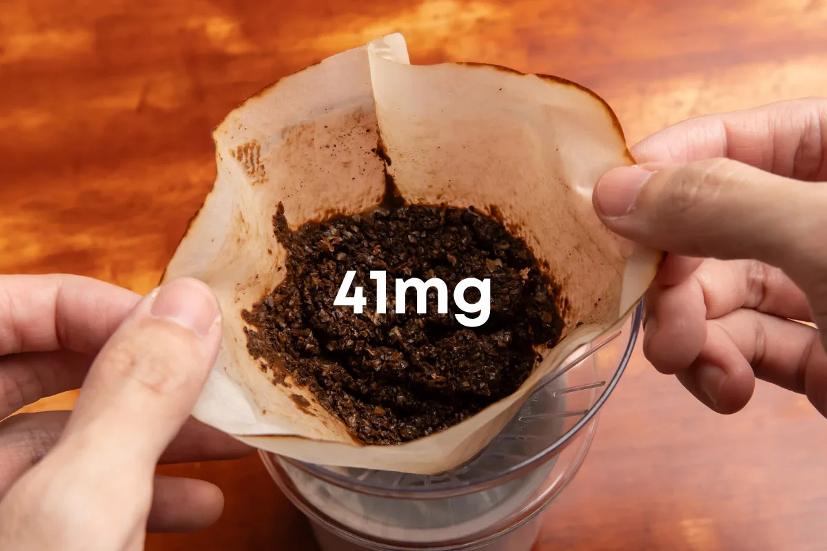 Man's hands holding a paper filter filled with used coffee grounds. text 41mg
