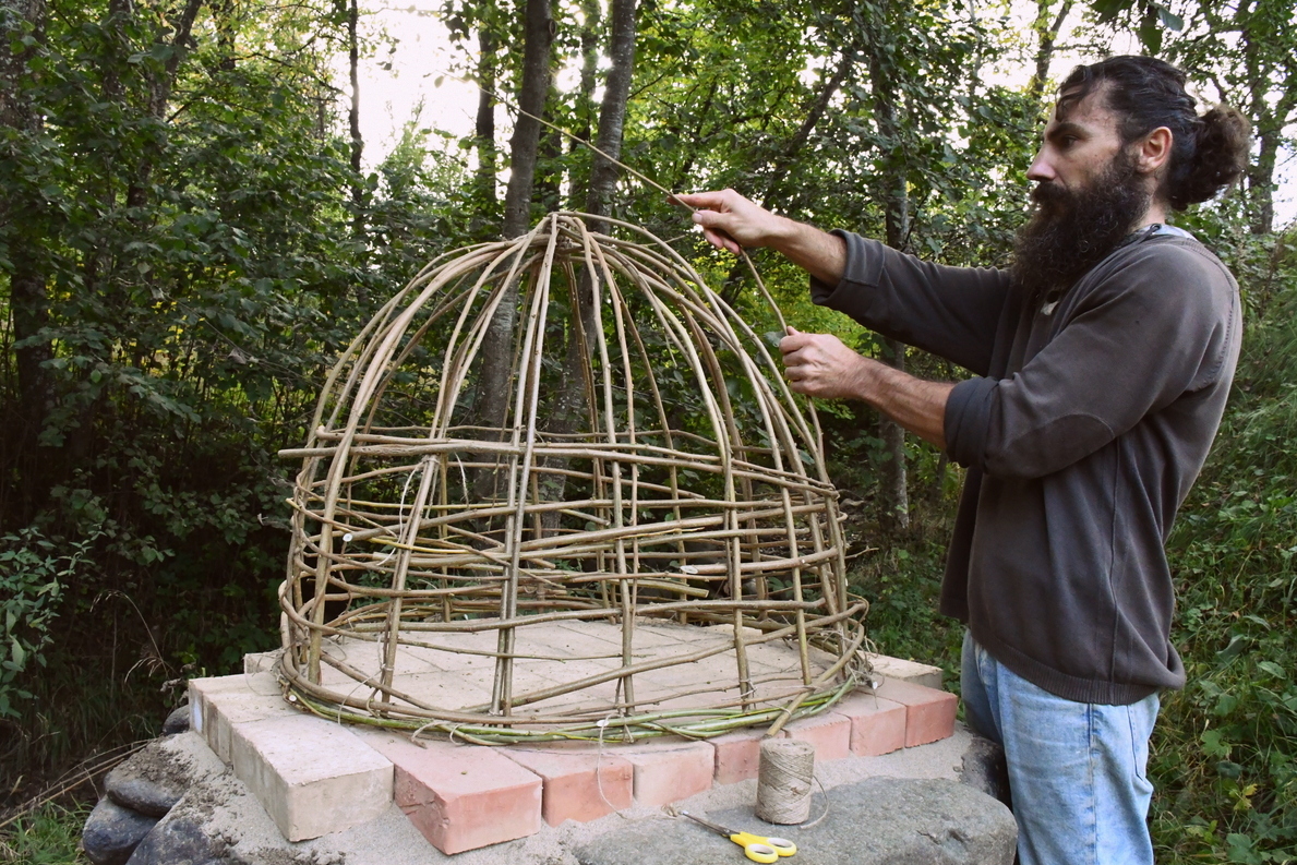 Man building frame of cob oven with willow branches