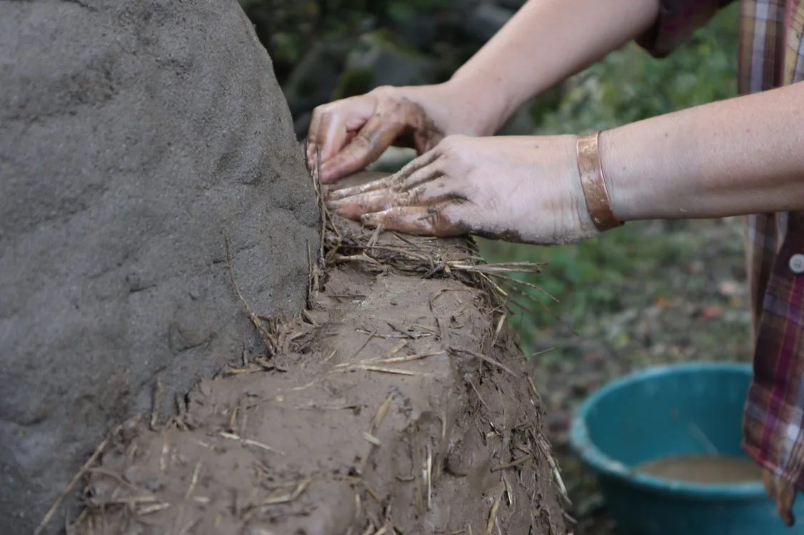 Woman's hands working hay into clay to make a cob oven