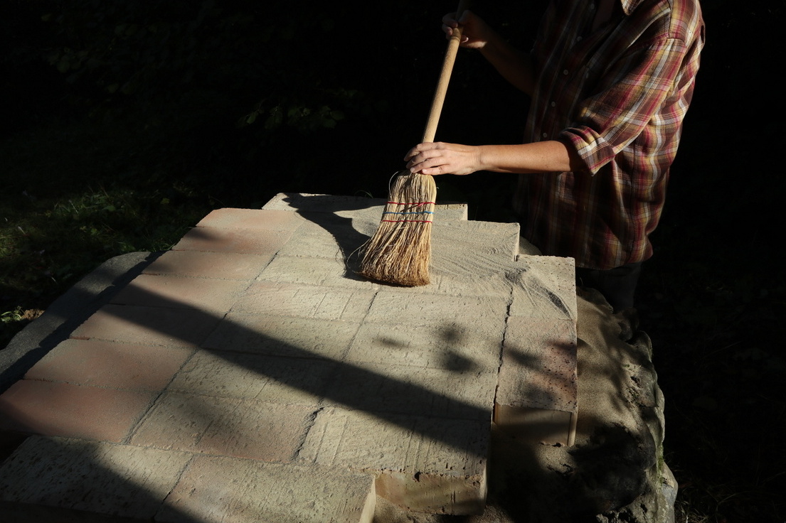Woman sweeping foundation of cob oven