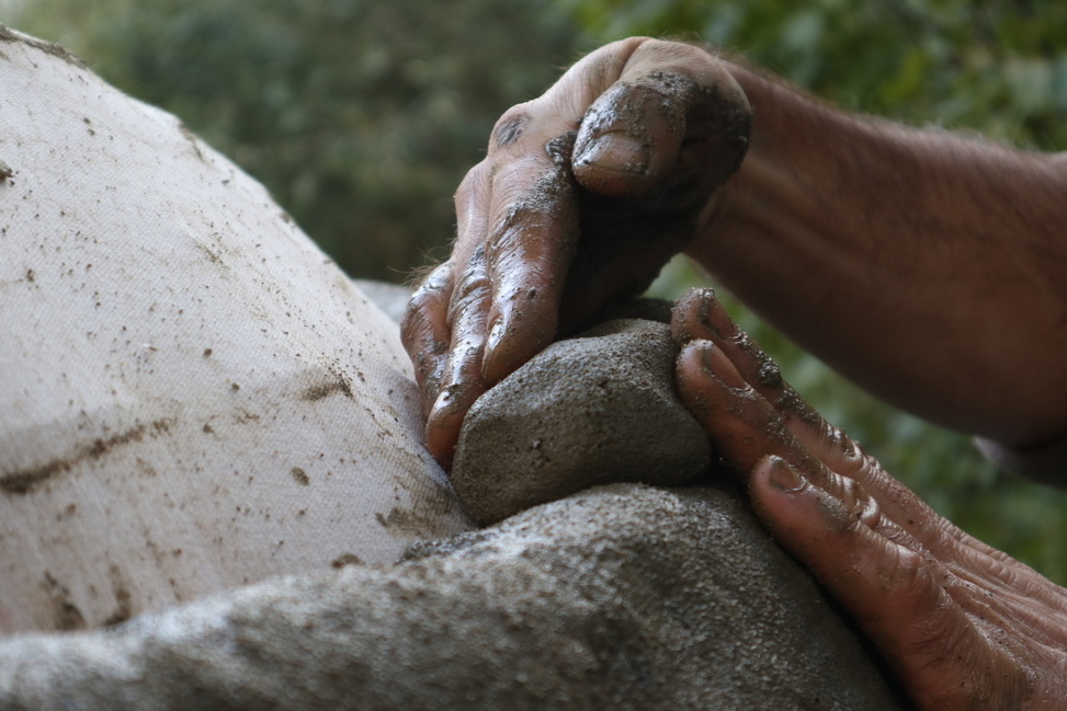 Hands molding clay layer on a cob oven