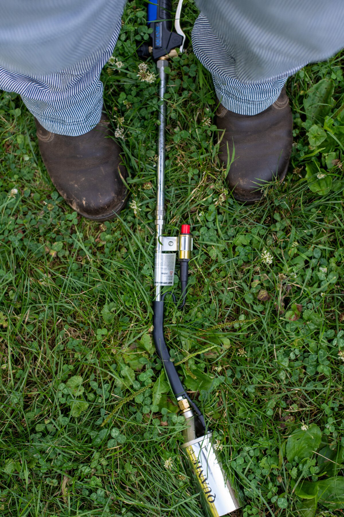 woman's boots and denim covered legs with a propane torch lying in the grass