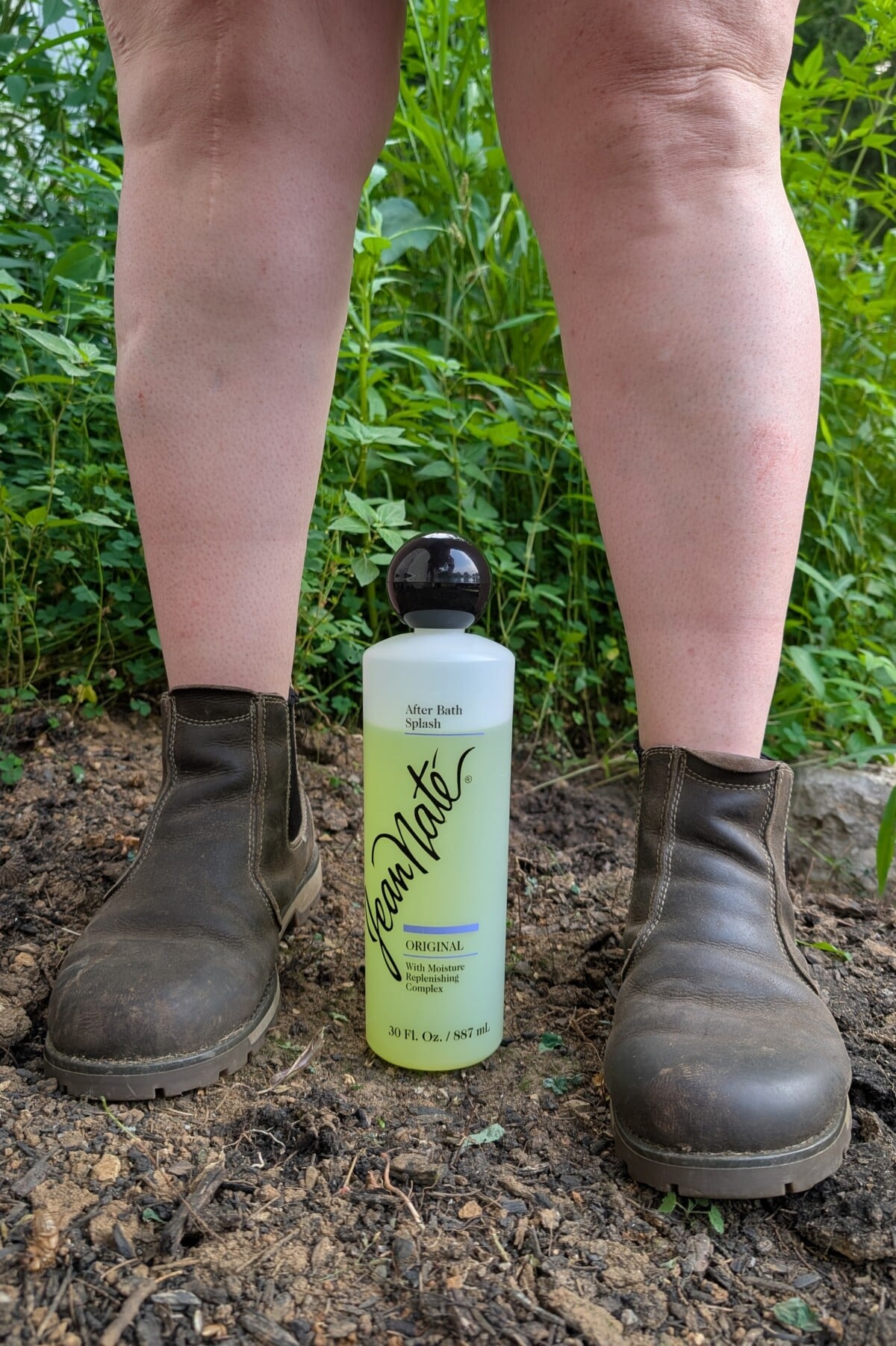 Woman's feet standing in flower bed with bottle of Jean Nate between her feet.