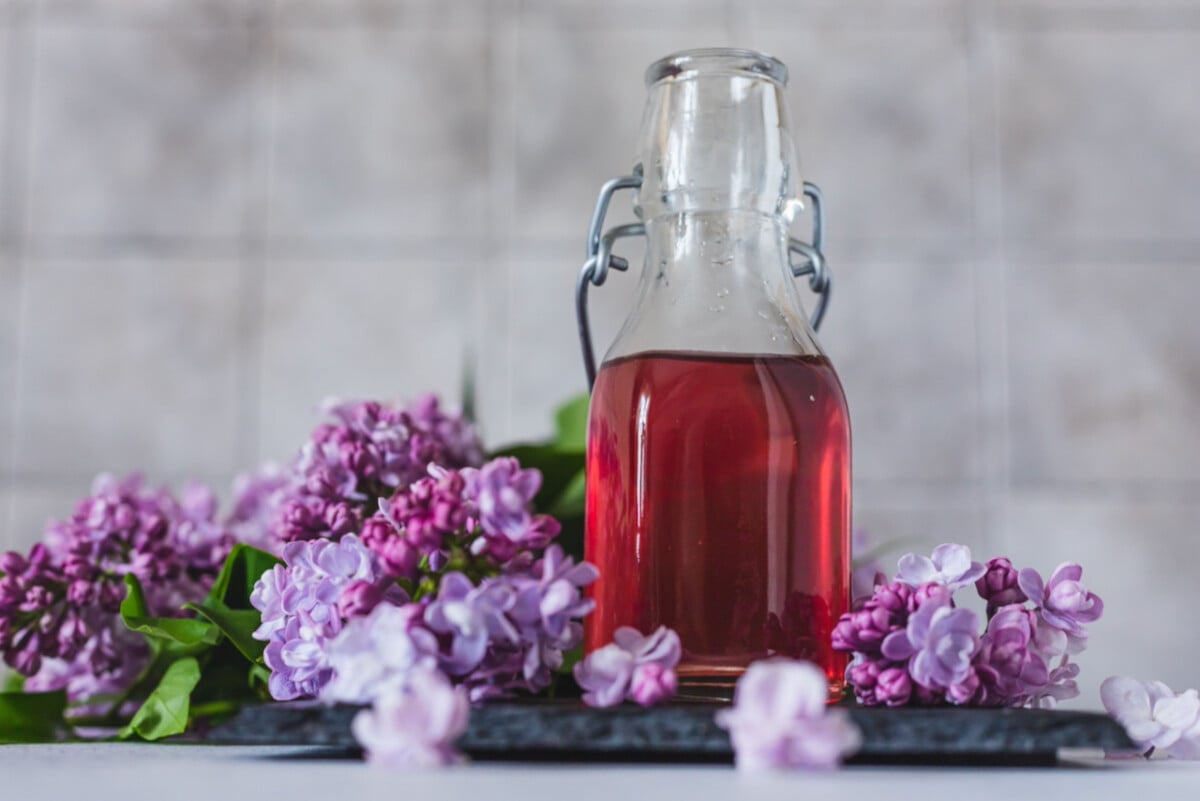 A bottle of lilac syrup with lilac flowers.