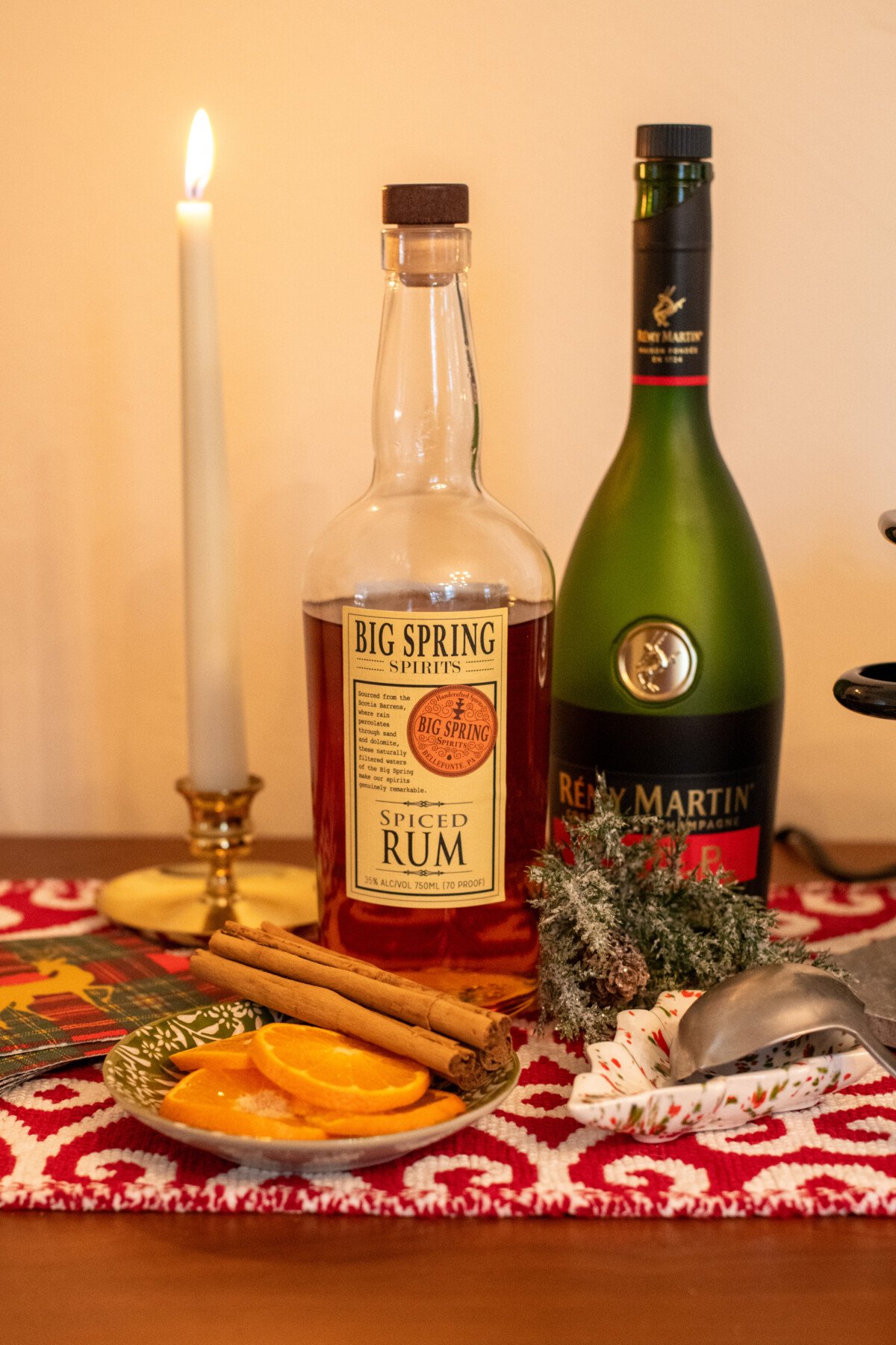 Bottles of spiced rum and cognac next to orange slice and cinnamon stick garnishes