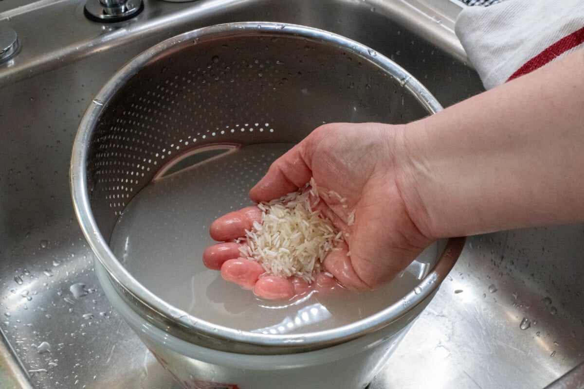 Woman's hand holding wet rice in rinse water