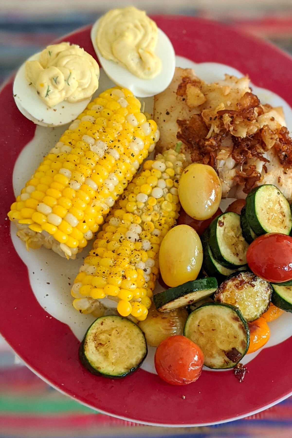 A plate with deviled eggs, fish, stir-fried vegetables and sweet corn.
