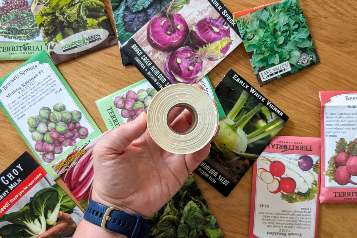 Woman's hand holding SmartSolve water soluble tape above packets of seeds