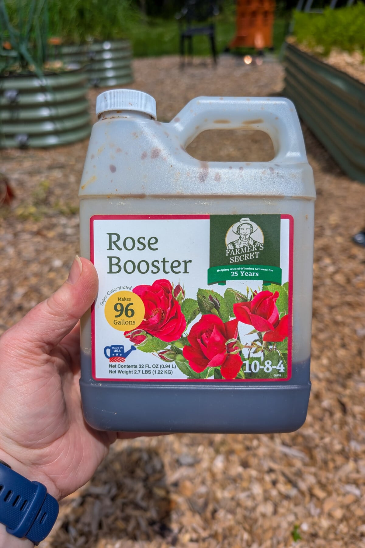 Hand holding a bottle of Farmer's Secret Rose Booster fertilizer. 